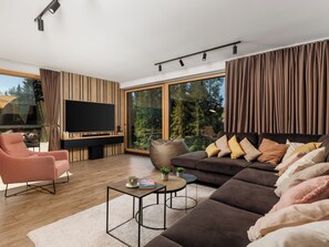 A modern living room with a large flat-screen TV, a sofa, a chair, and a coffee table. - Valera Vita Forest by Interhome (Skrad)