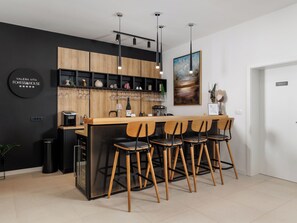 Zona de bar moderna amb un taulell de fusta, cadires negres i una paret negra amb prestatgeries.