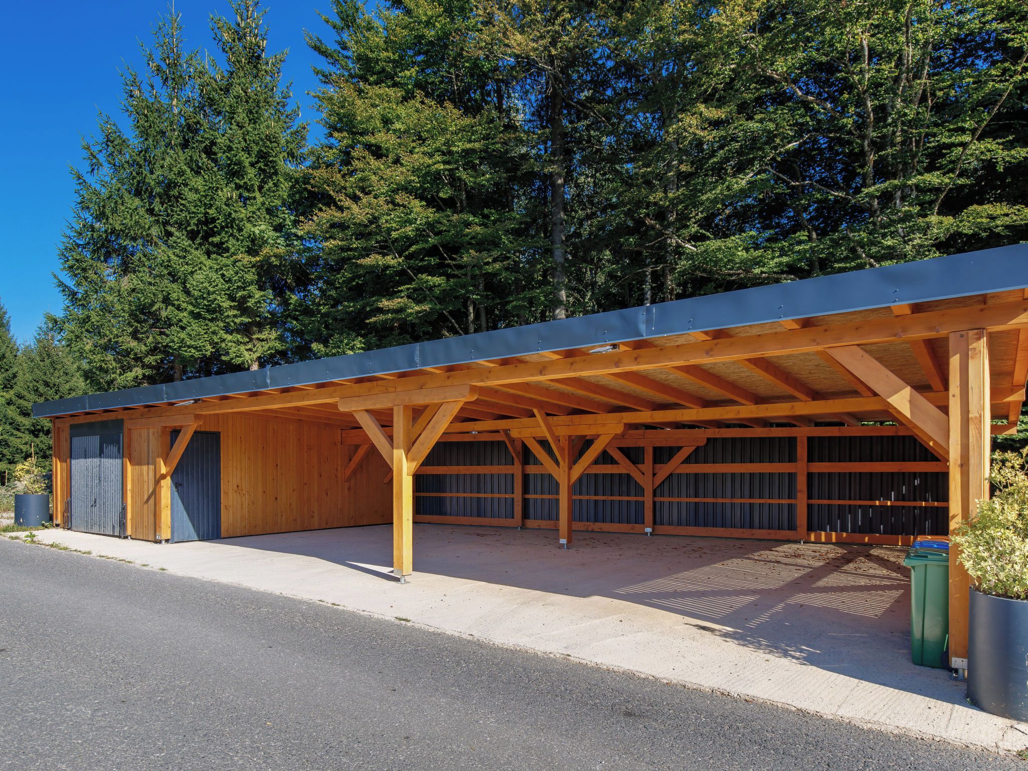 A covered parking structure with multiple garage doors, surrounded by trees.