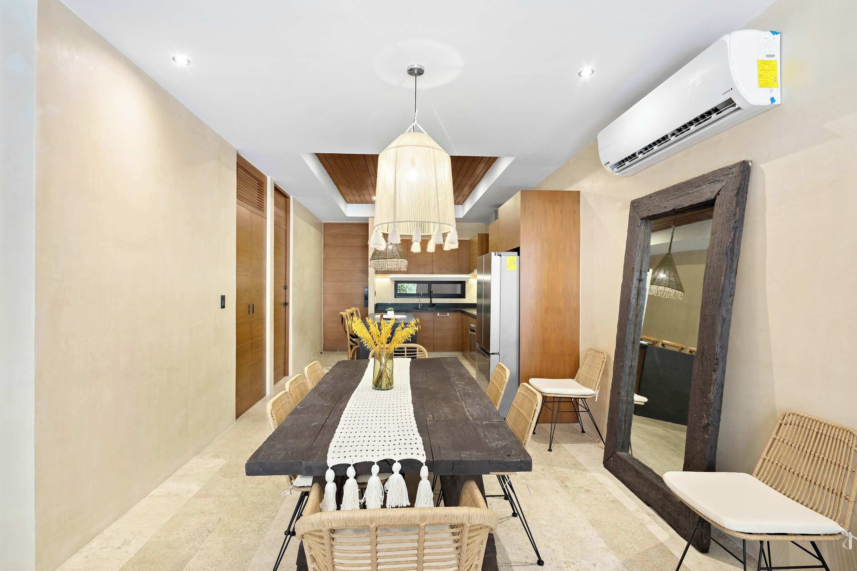 A modern dining area with a long table, chairs, a chandelier, and an air conditioning unit.