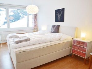 A bedroom with a bed, bedside table, and a window with a view of snow-covered mountains. - Tgesa Sunnmatt 24 Appartement/Fewo, Bad, WC, 1 Schlafraum by Interhome (Savognin)