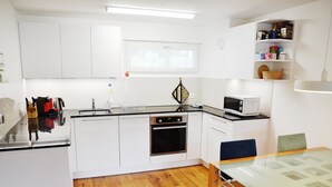 Uma cozinha moderna com armários brancos, micro-ondas, fogão e uma área de refeições com mesa e cadeiras de vidro.