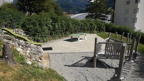 Um parquinho com escorrega, mesa de pingue-pongue e uma estrutura de escalada de madeira.