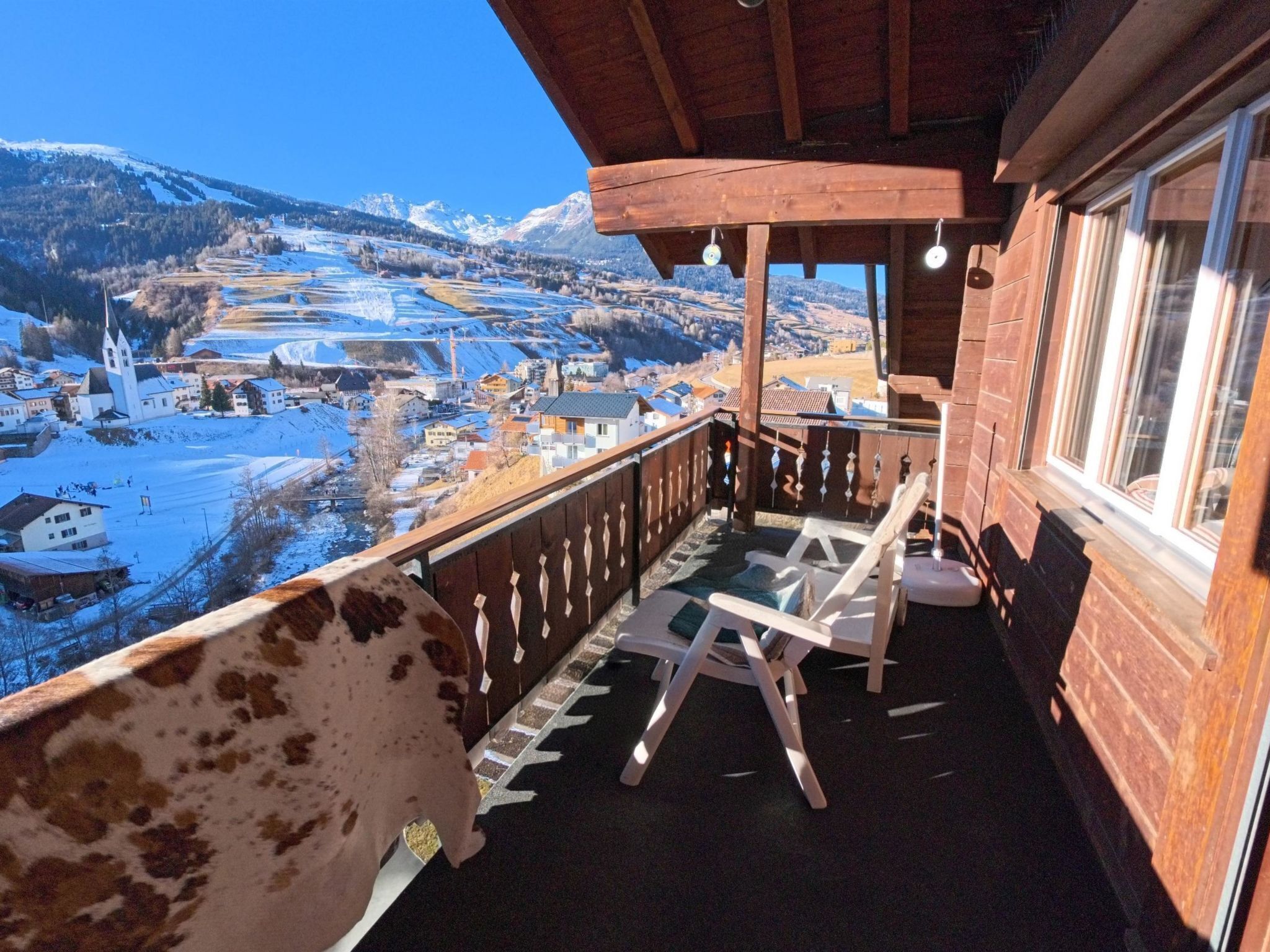 A wooden balcony with a view of a snow-covered landscape and a church.
