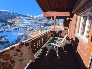 A wooden balcony with a view of a snow-covered landscape and a church. - Chalet Rezia Appartement/Fewo, Dusche oder Bad, WC, 1 Schlafraum by Interhome (Savognin)
