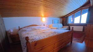 En säng i trä med ett mönstrat överkast i ett rum med träväggar och ett sluttande tak.