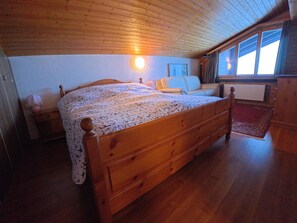A wooden bed with a patterned bedspread in a room with wooden walls and a sloped ceiling. - Chalet Rezia Appartement/Fewo, Dusche oder Bad, WC, 1 Schlafraum by Interhome (Savognin)