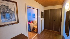 En hall med trägolv, en inramad tavla på vänster sida och en dörr som leder till ett rum med en soffa och ett litet bord.
