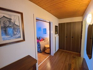 A hallway with wooden flooring, a framed painting on the left, and a door leading to a room with a sofa and a small table. - Chalet Rezia Appartement/Fewo, Dusche oder Bad, WC, 1 Schlafraum by Interhome (Savognin)