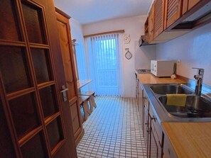 A compact kitchen with a tiled floor, wooden cabinets, a microwave, and a sink. - Chalet Rezia Appartement/Fewo, Dusche oder Bad, WC, 1 Schlafraum by Interhome (Savognin)