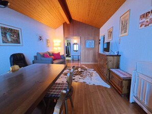 A cozy living room with a wooden ceiling, a dining table with chairs, a sofa with cushions, a cowhide rug, and a television on a wooden cabinet. - Chalet Rezia Appartement/Fewo, Dusche oder Bad, WC, 1 Schlafraum by Interhome (Savognin)