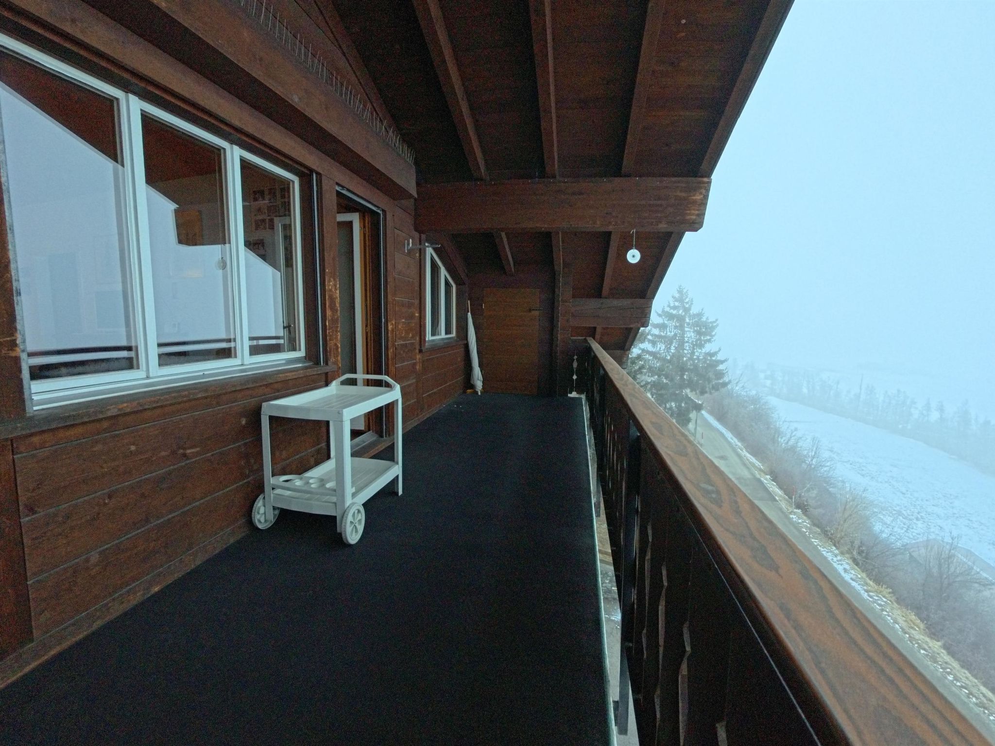 Ein hölzerner Balkon mit einem weißen Wagen, großen Fenstern und Blick auf eine verschneite Landschaft.
