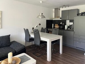 A modern kitchen with a dining area, grey cabinets, and a white table. - Tgesa Tgampi T20 Appartement/Fewo, Dusche, WC, 2 Schlafräume by Interhome (Savognin)