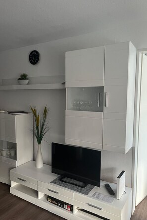 A modern living room with a flat-screen TV, white cabinetry, a clock, and a plant. - Tgesa Tgampi T20 Appartement/Fewo, Dusche, WC, 2 Schlafräume by Interhome (Savognin)