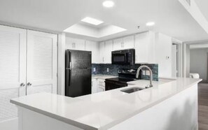 Una cucina moderna con mobili bianchi, un frigorifero nero, un forno a microonde e una grande isola con lavello.