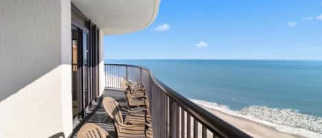 A balcony with wooden chairs facing the ocean.