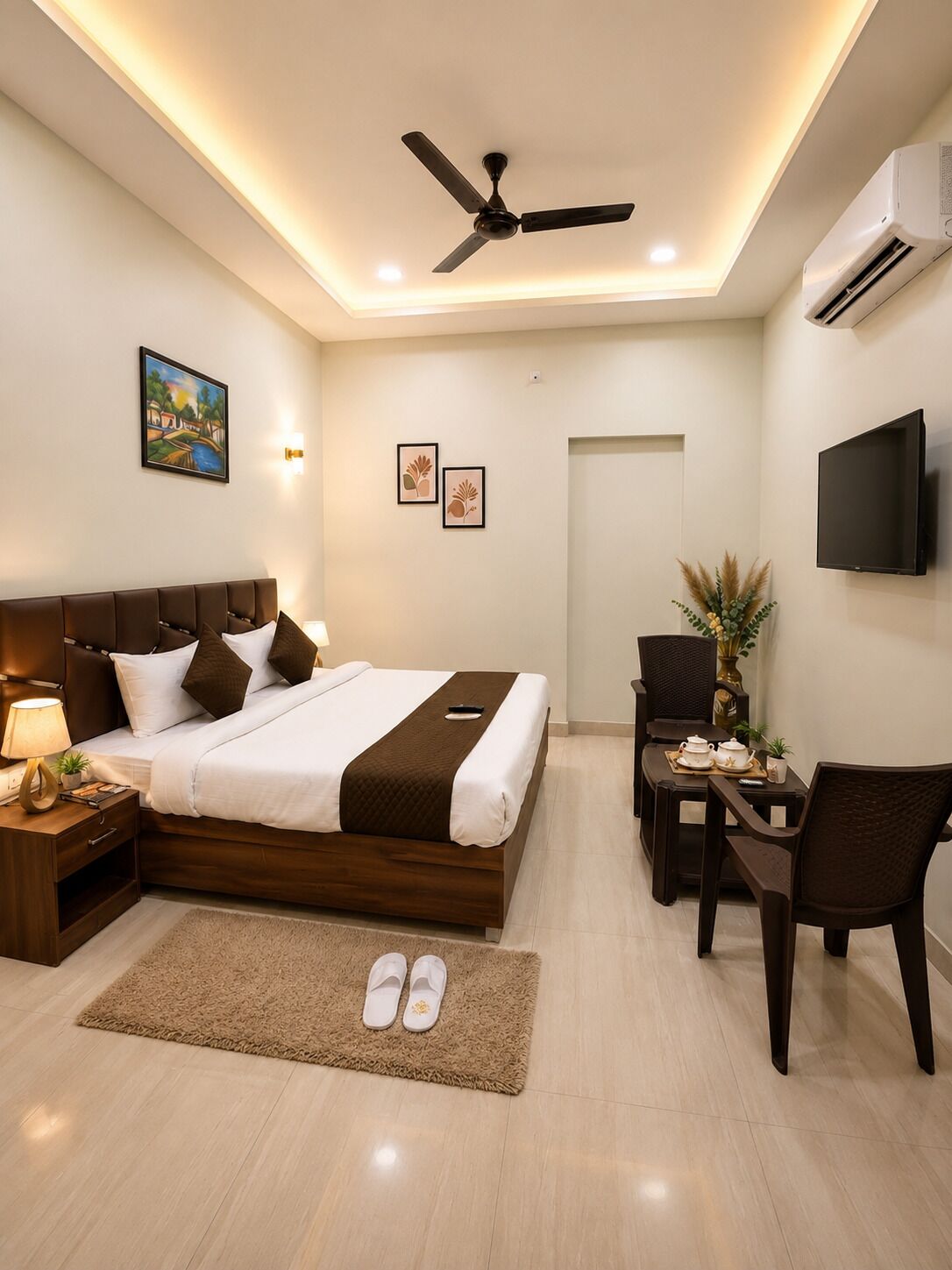 A hotel room with a bed, bedside table, lamp, TV, and a desk with chairs.