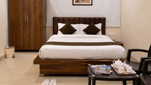 Een hotelkamer met een bed, een plafondventilator, een airconditioningapparaat, een houten garderobe en een kleine tafel met een dienblad en kopjes.