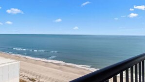 A coastal view from a balcony with a railing, overlooking a beach and the ocean. - Compass Cove Beachfront Escape | Pool Access | Balcony | Hot Tub | Free Parking (Myrtle Beach)