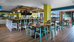 A modern restaurant with wooden floors, teal chairs, and a bar area. - Compass Cove Beachfront Escape | Pool Access | Balcony | Hot Tub | Free Parking (Myrtle Beach)