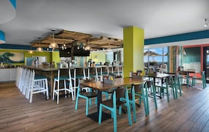 En modern restaurang med trägolv, stolar i turkos färg och en bardisk.
