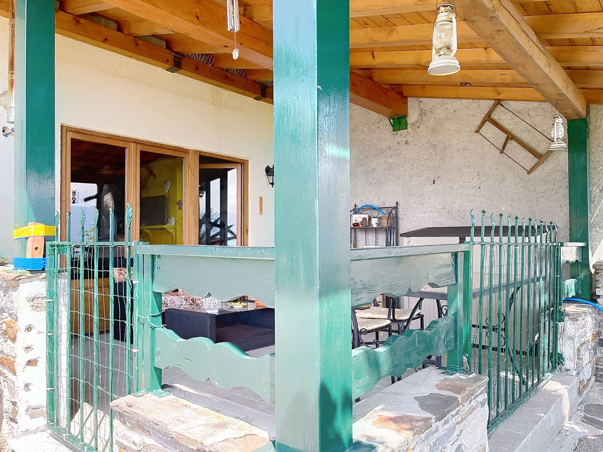 A covered outdoor area with a wooden ceiling, a metal fence, and a stone wall.