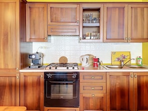 A kitchen with wooden cabinets, a gas stove, an oven, a coffee maker, and a sink. - Baita Melissa by Interhome (Vercana)