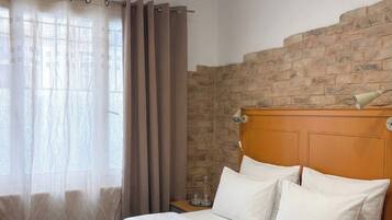A hotel room with a neatly made bed, a headboard with a stone-like texture, and a window with sheer curtains.