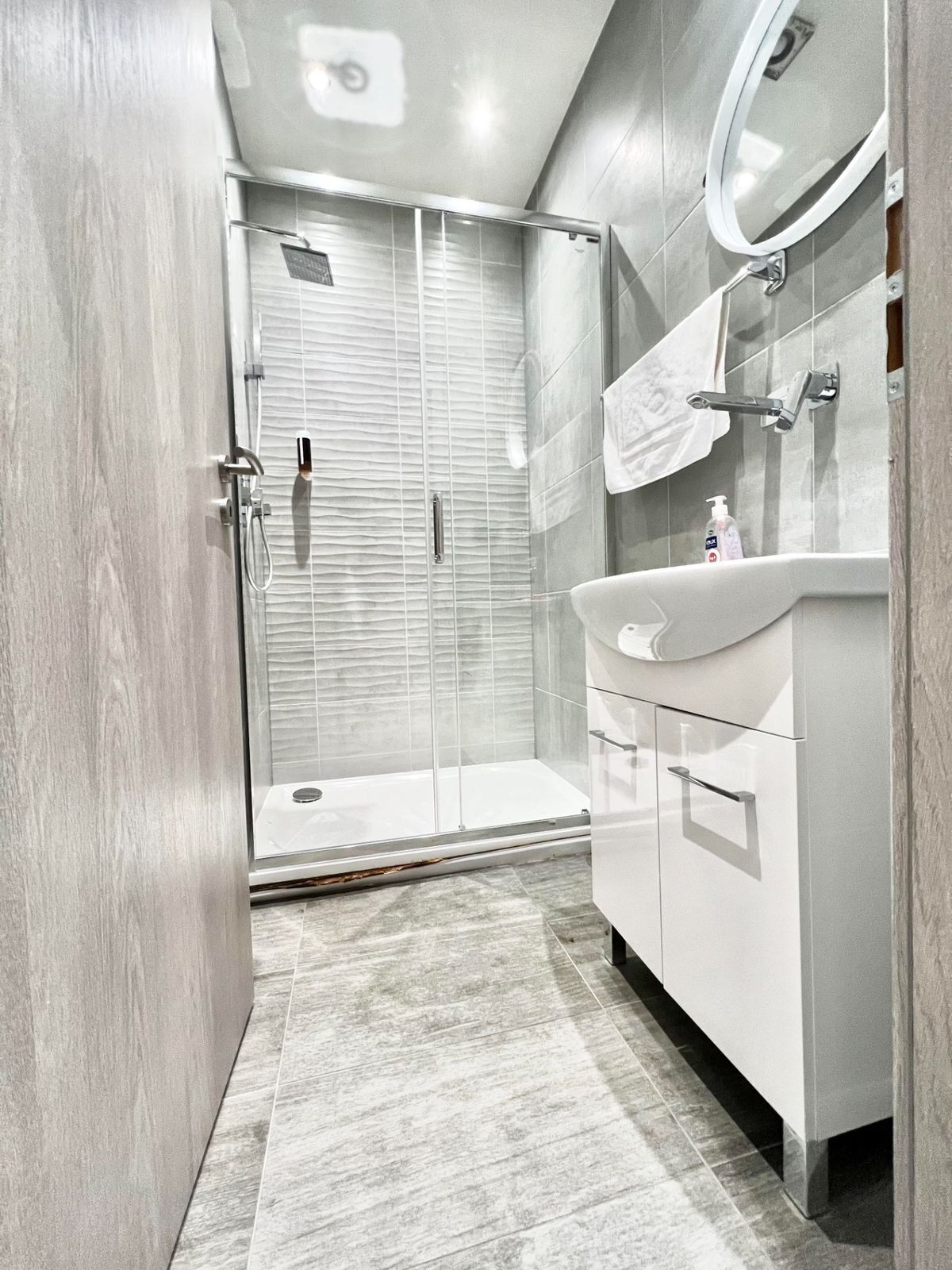 Une salle de bain moderne avec une douche à parois de verre, un meuble-lavabo blanc avec un miroir et un sol carrelé.