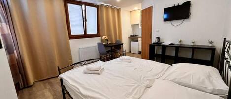 A bedroom with a bed, a desk, a chair, a television, and a radiator.