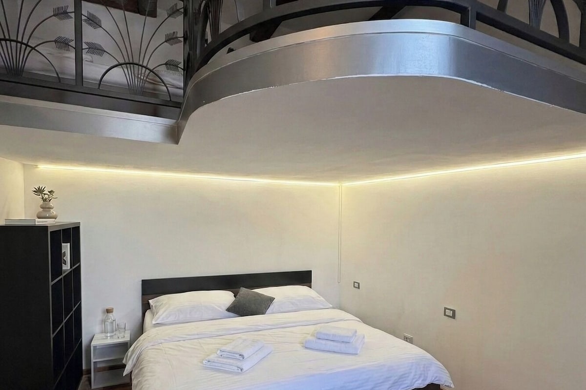 A bedroom with a curved ceiling, a bed with white linens, a nightstand, and a wooden floor.