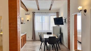 Un comedor con una mesa y sillas, un televisor montado en la pared y un pilar de ladrillo.