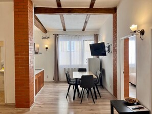A dining area with a table and chairs, a television mounted on the wall, and a brick column. - Celeste Prague (Hlavní město Praha)