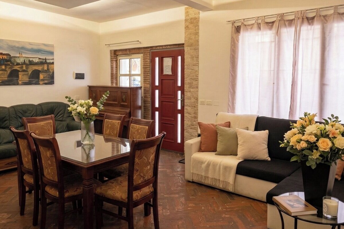 A living room with a dining table, chairs, a sofa, and a window with curtains.