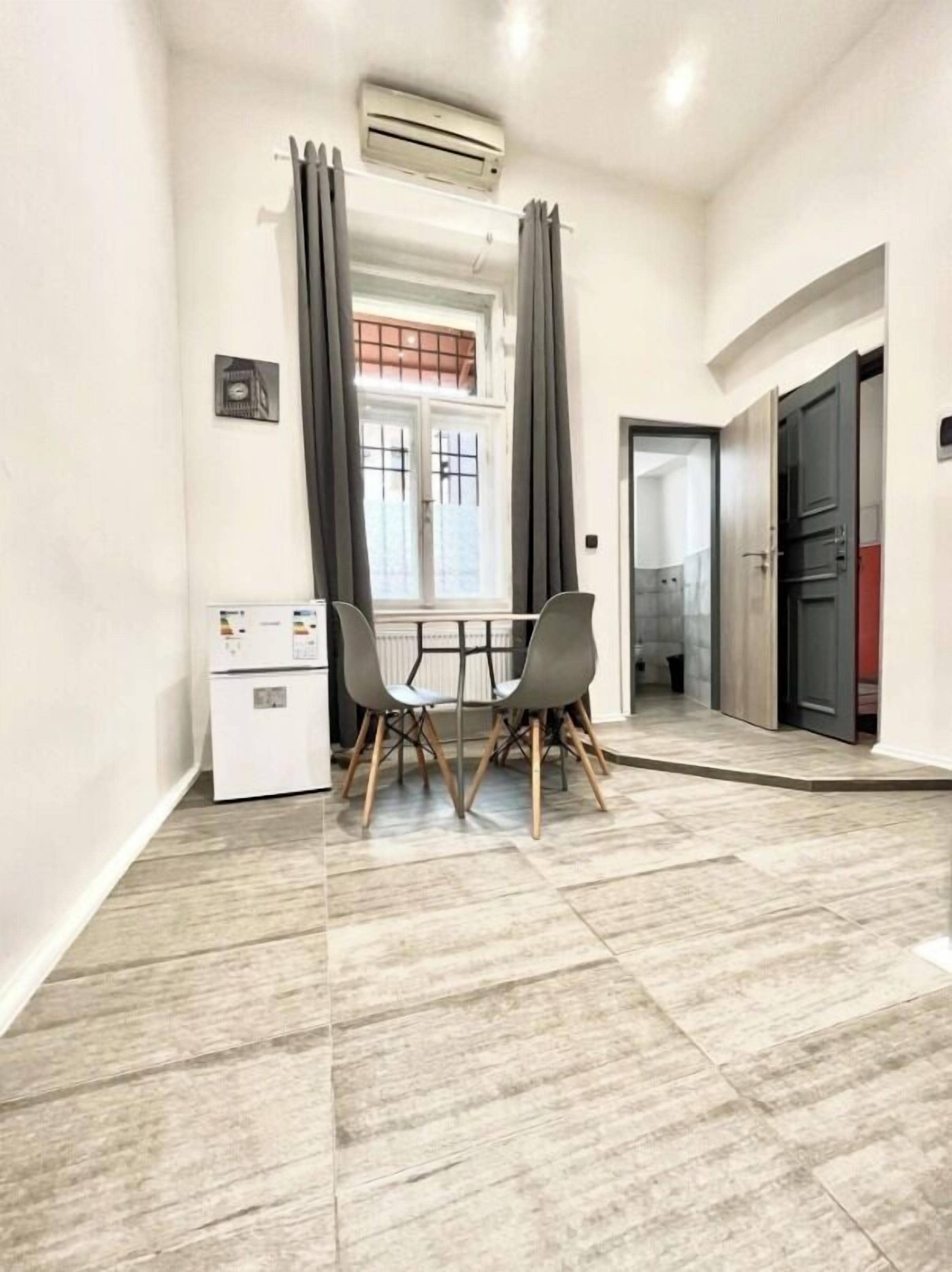 A room with a dining table and chairs, a small kitchenette, and a sliding door leading to another room.