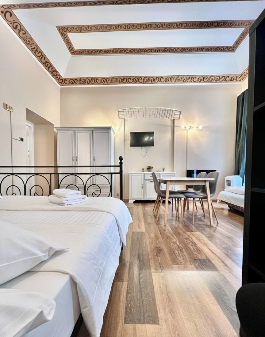 A hotel room with a bed, a desk, and a chair. There is a television on the wall and a wardrobe.