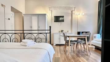A hotel room with a bed, a desk, and a chair. There is a television on the wall and a wardrobe.
