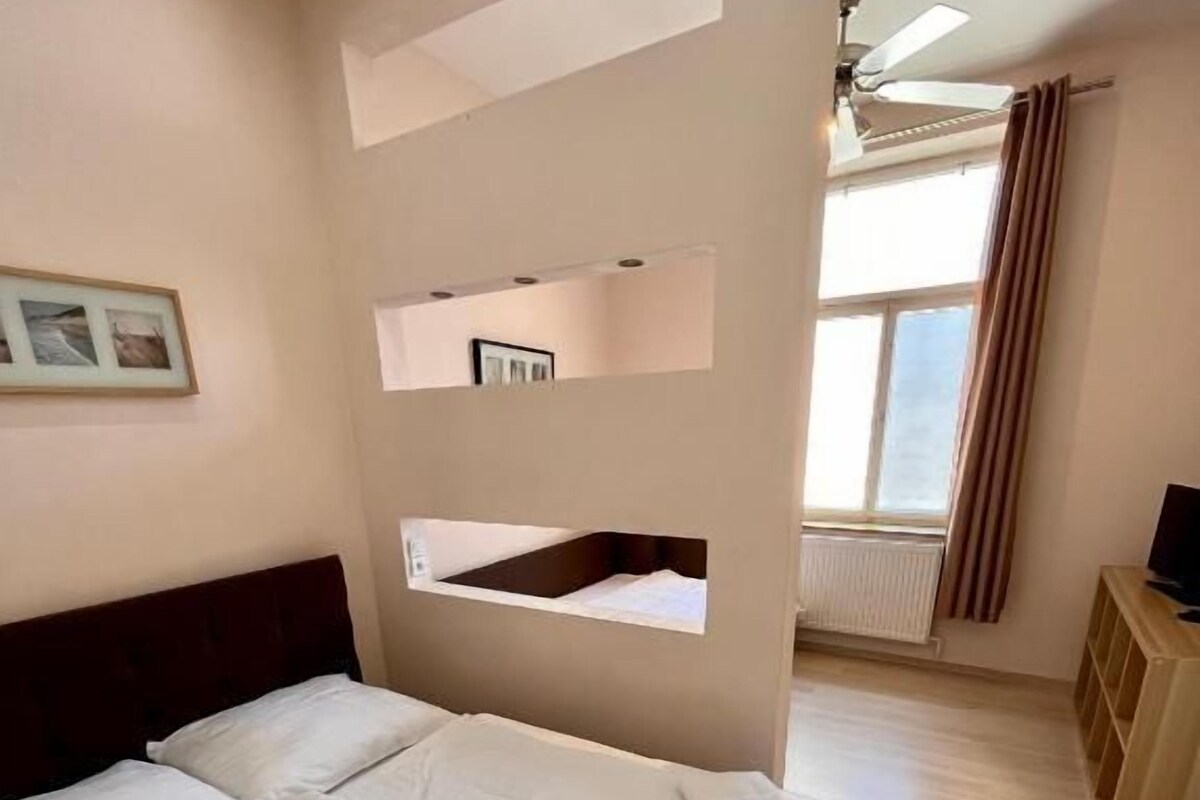 A bedroom with a bed, a ceiling fan, a window with curtains, and a radiator.