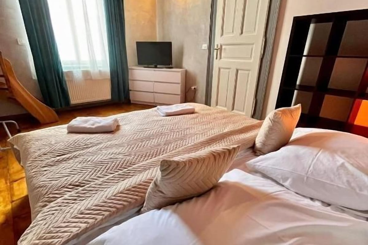 Un dormitorio con cama, almohadas, televisor, cómoda y una puerta.