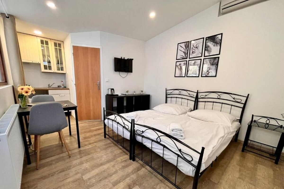 A bedroom with a bed, a desk, and a chair. There is a television on the wall and a window.