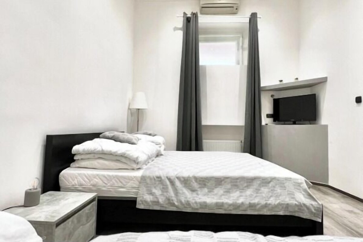 Una habitación de hotel con dos camas, un televisor de pantalla plana, una mesita de noche, una lámpara y un equipo de aire acondicionado.