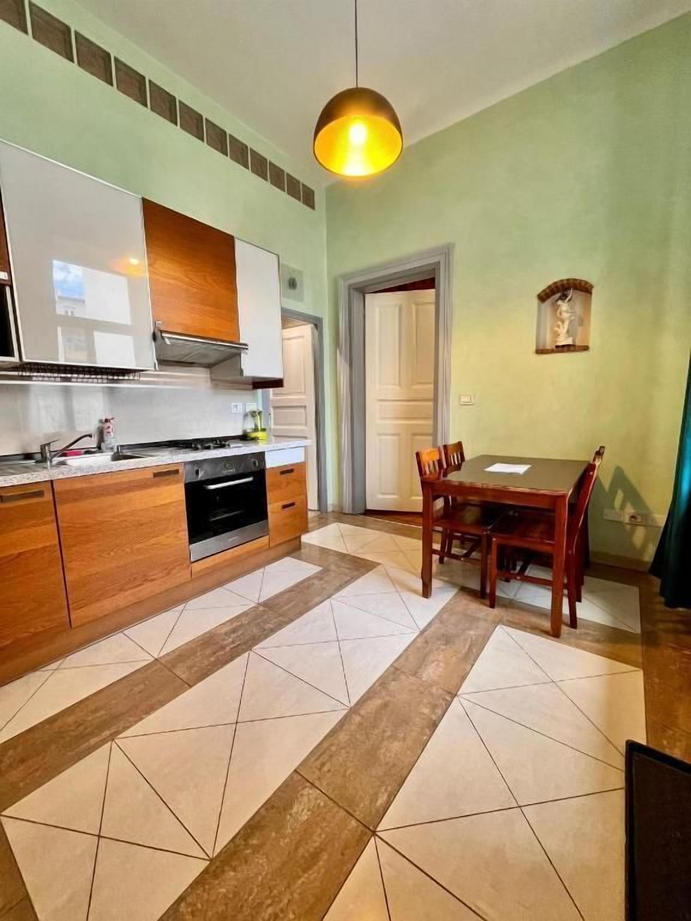A compact kitchen with a dining area, featuring a built-in oven, a sink, and a dining table with chairs.