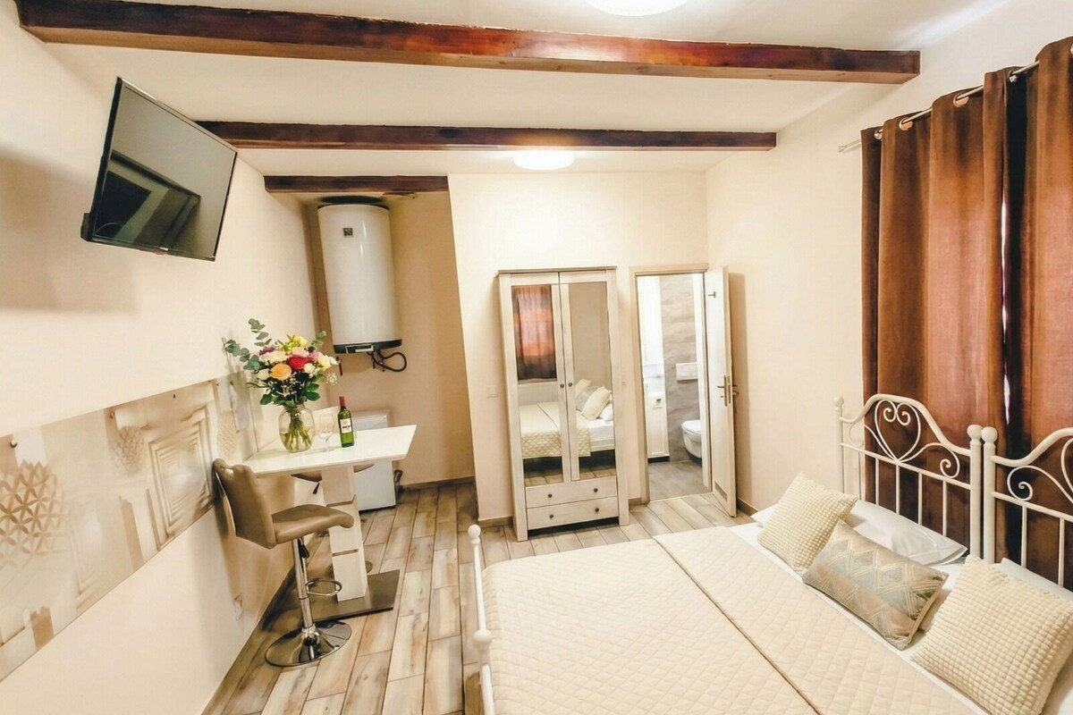 A bedroom with a bed, bedside table, mirror, wardrobe, and a TV mounted on the wall.