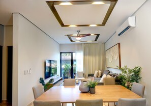 A modern dining area with a wooden table, chairs, a ceiling fan, and a large window with curtains. - Luxury Condo at Amira District Rooftop Infinity (Tulum Municipality)