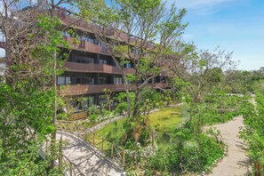 A multi-story building with balconies, surrounded by greenery and a small pond. - Luxury Condo at Amira District Rooftop Infinity (Tulum Municipality)