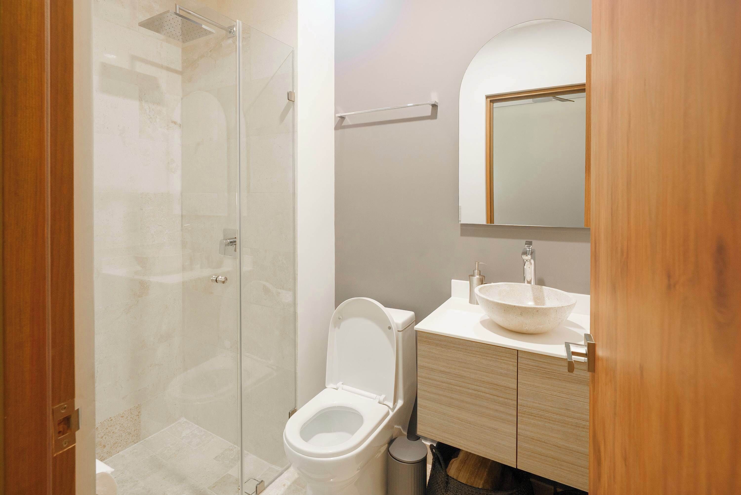 A bathroom with a glass shower enclosure, a toilet, a sink with a mirror above it, and wooden cabinetry.