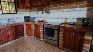 Une cuisine avec des meubles de rangement en bois, une cuisinière, un évier et une fenêtre avec des barreaux.