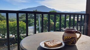 Une table avec une assiette de toasts et une tasse en céramique, placée sur un balcon donnant sur un paysage montagneux.