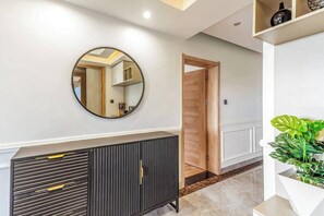 A hallway with a round mirror, a wooden door, a black cabinet, and a potted plant. - Urban Oasis (Nairobi)