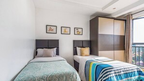 Habitación de hotel con dos camas individuales, un ventanal con cortinas y tres cuadros en la pared.